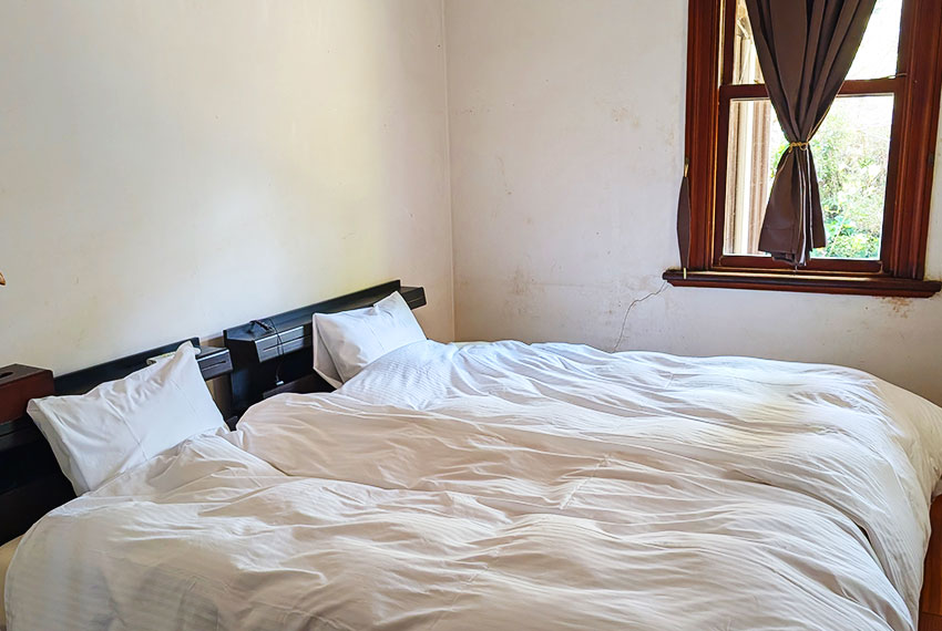 昭和レトロな洋室に並ぶシングルベッドと木枠の窓から差し込む自然光